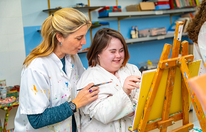 Teacher helping a woman with down syndrome during painting class